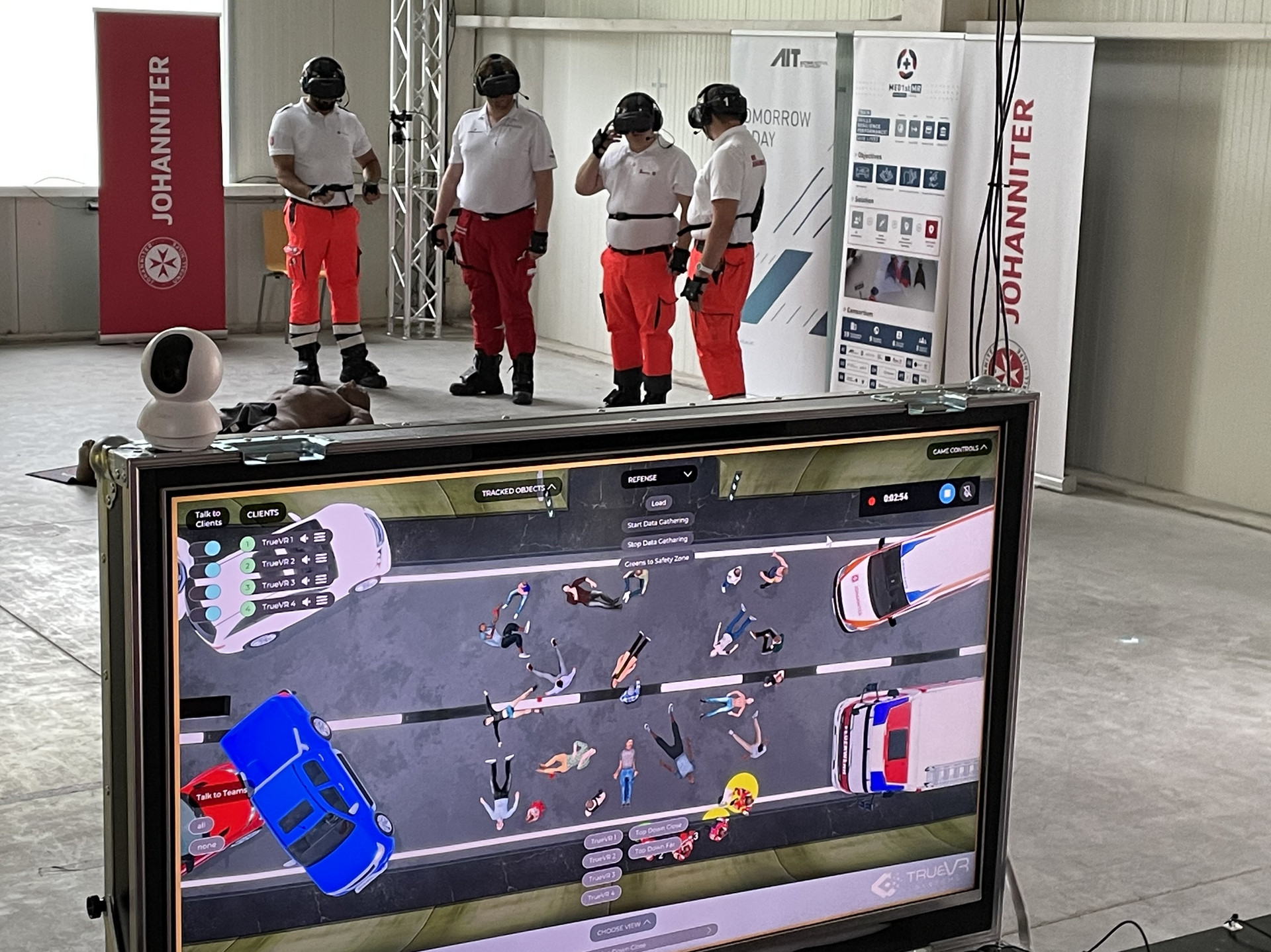 im Hintergrund sind vier Personen mit VR-Brillen zu sehen, ihre Bewegungen werden in ein Trainingsszenario auf einem Bildschirm übertragen