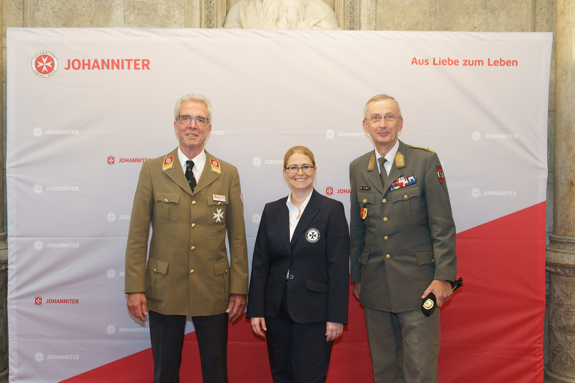 Präsident Johannes Bucher und Bundesgeschäftsführerin Petra Grell-Kunzinger mit Personen vor einer Johanniter Leinwand