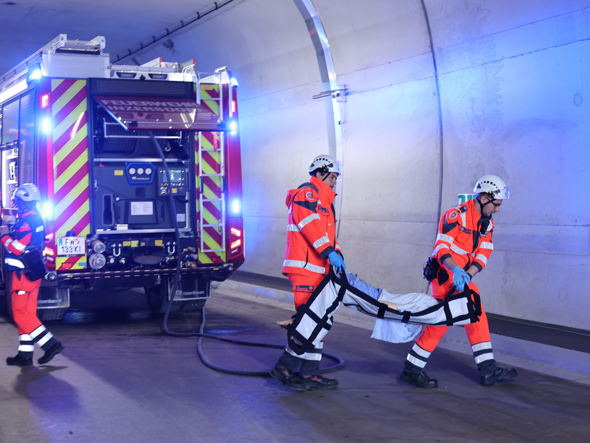 zwei Sanitäter tragen eine Übungspuppe, im Hintergrund sieht man ein Feuerwehrauto mit Blaulicht
