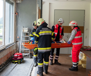 Sanitäter heben die verletzte Person auf einer Trage um sie durch das Fenster vom Unfallort wegzubringen.