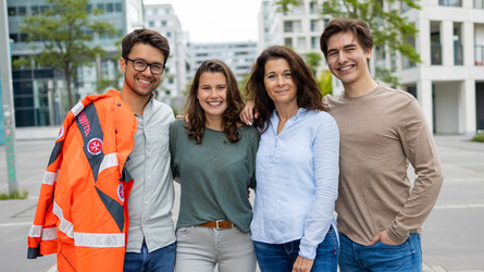 Vier Ehrenamtliche stehen Arm in Arm nebeneinander. Einer davon trägt eine Einsatzjacke des Rettungsdienstes.