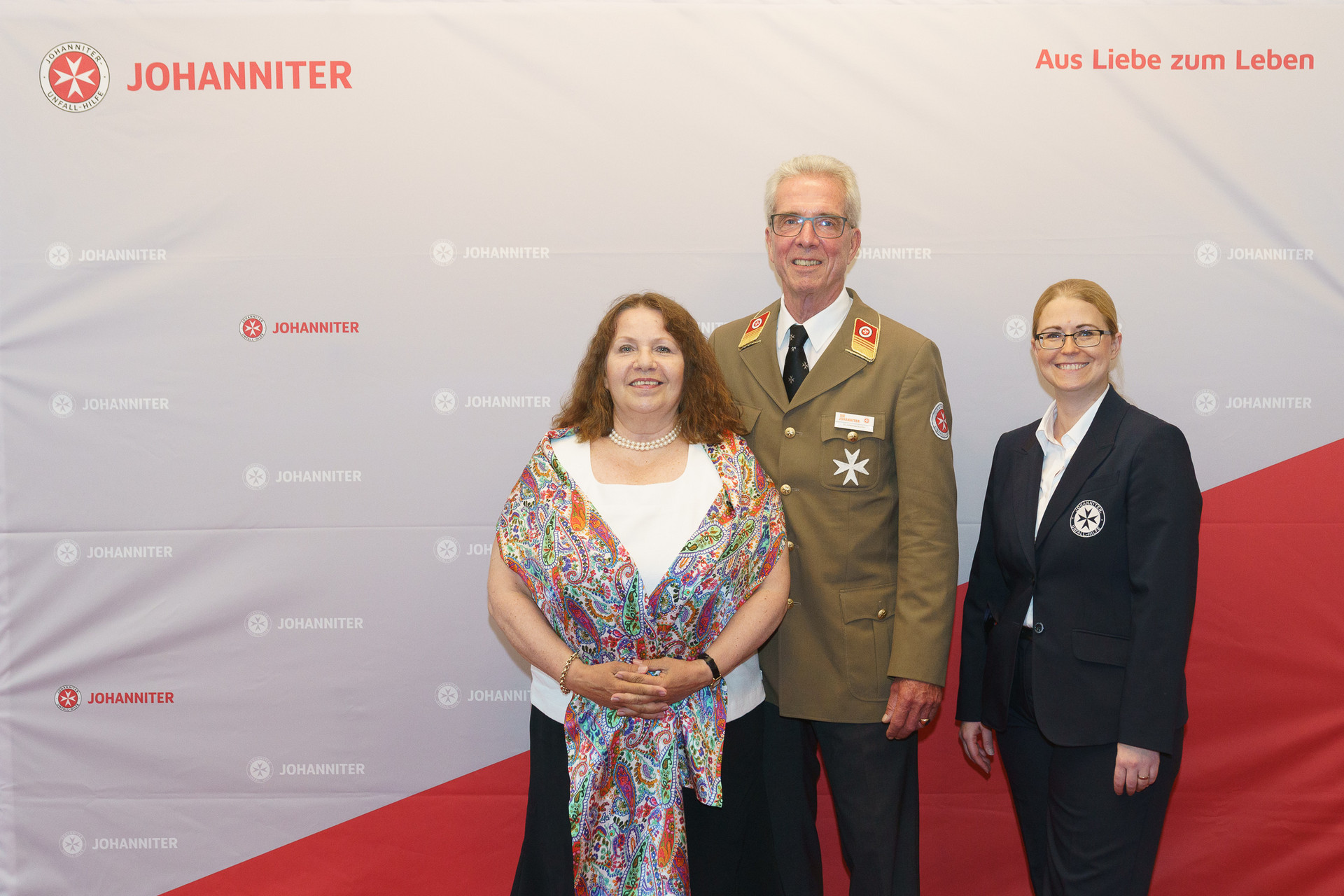 Präsident Johannes Bucher und Bundesgeschäftsführerin Petra Grell-Kunzinger mit Personen vor einer Johanniter Leinwand