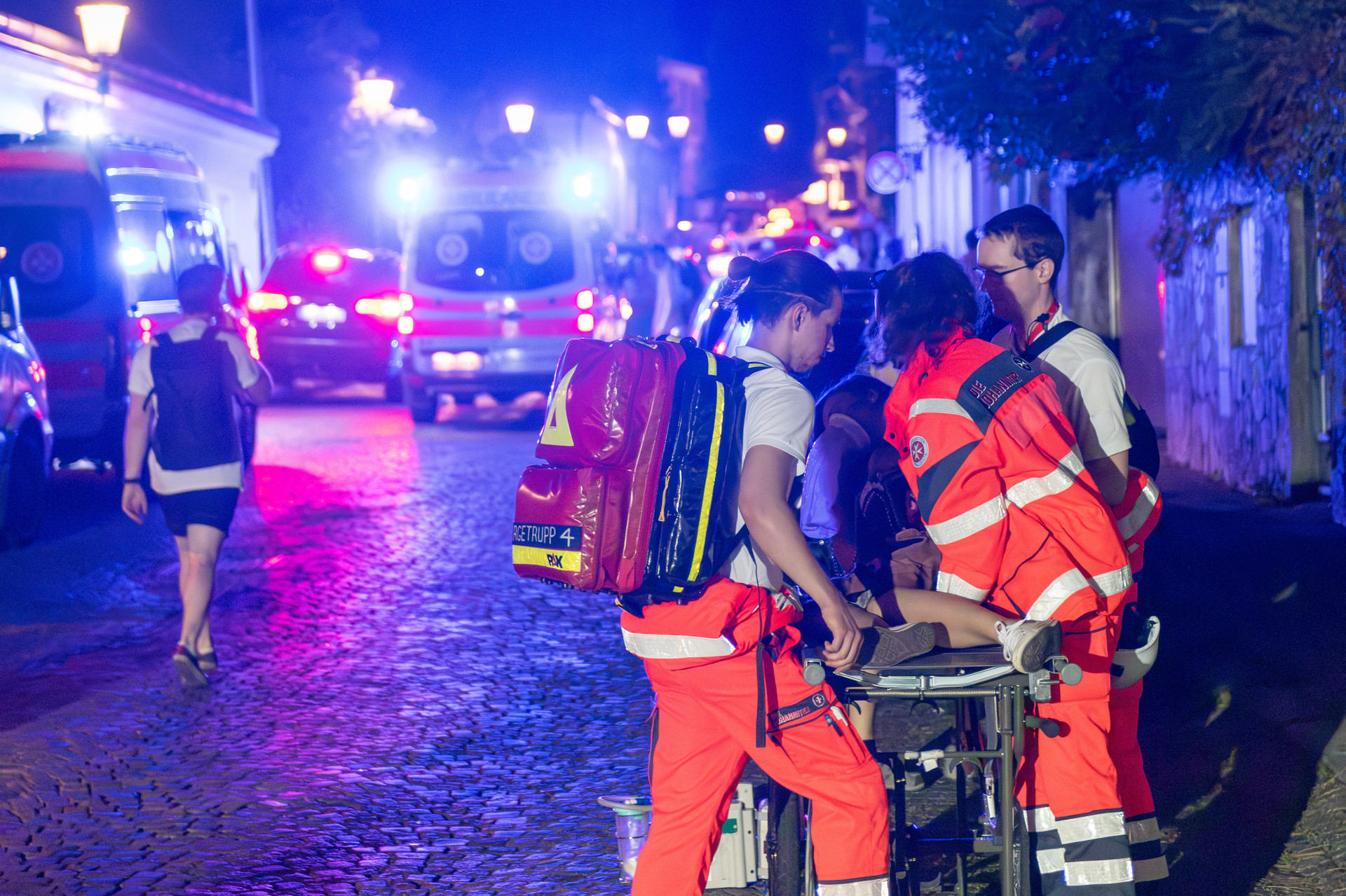 Ein Einsatzteam hilft einem Mädchen, das auf der Bergetrage liegt. Im Hintergrund fährt ein Krankenwagen mit Blaulicht.