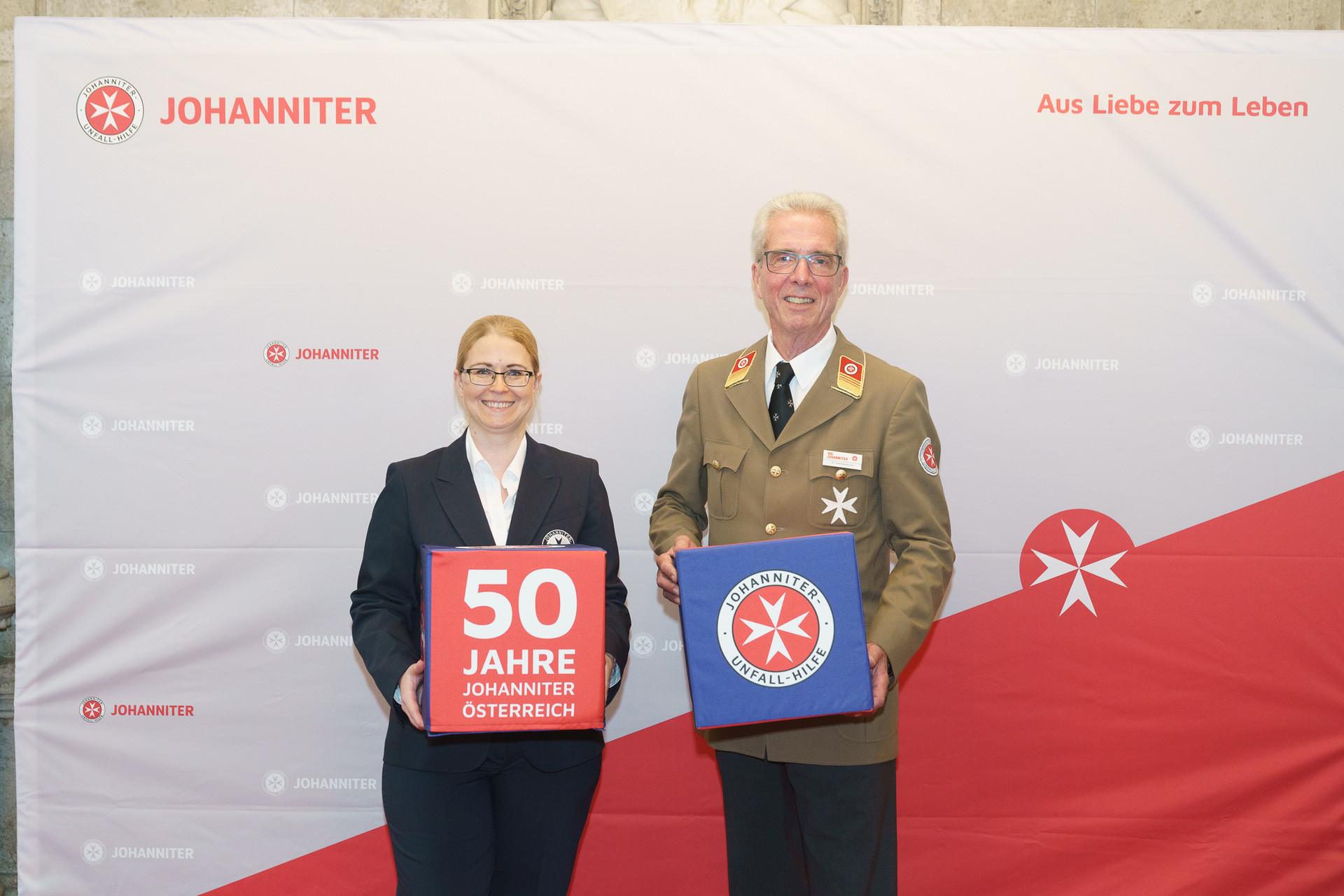 Präsident Johannes Bucher und Bundesgeschäftsführerin Petra Grell-Kunzinger vor einer Johanniter Leinwand