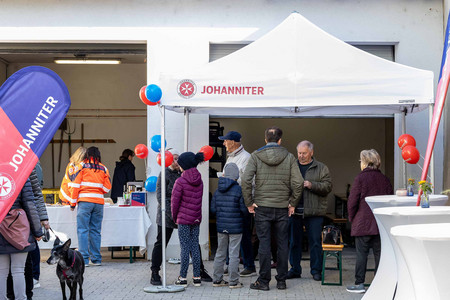 Gäste beim Tag der offenen Tür stehen im dekorierten Hof der Johanniter unter einem Zelt.
