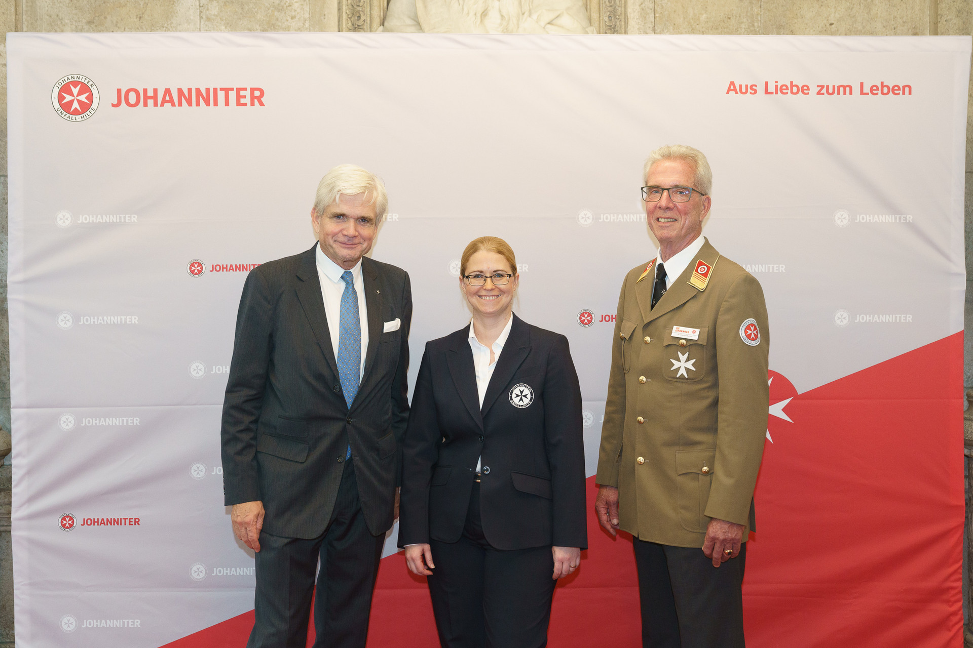 Präsident Johannes Bucher und Bundesgeschäftsführerin Petra Grell-Kunzinger mit Personen vor einer Johanniter Leinwand