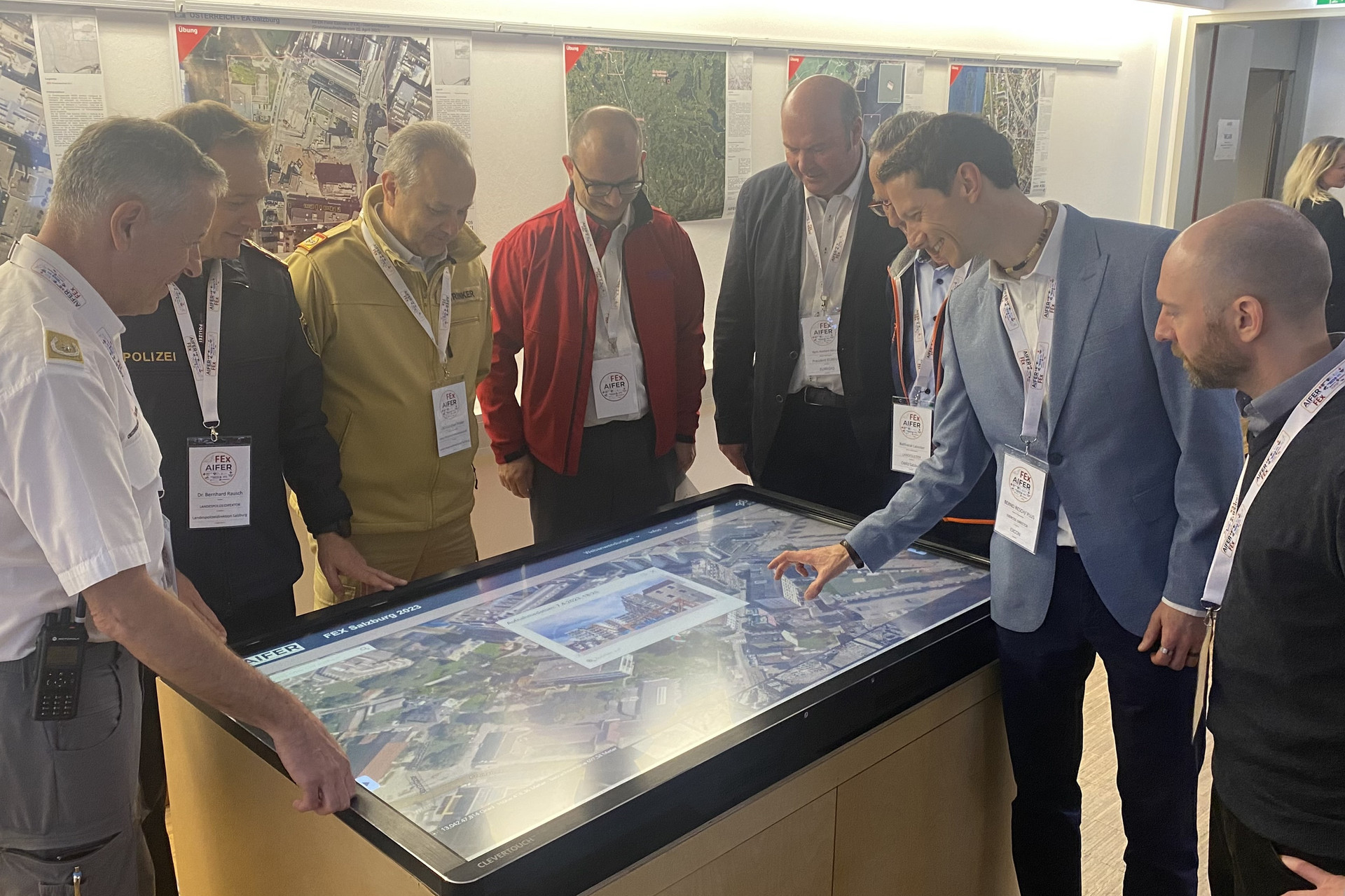 mehrere Personen stehen um einen großen Touchscreen herum, der eine Stadt in der Vogelperspektive zeigt