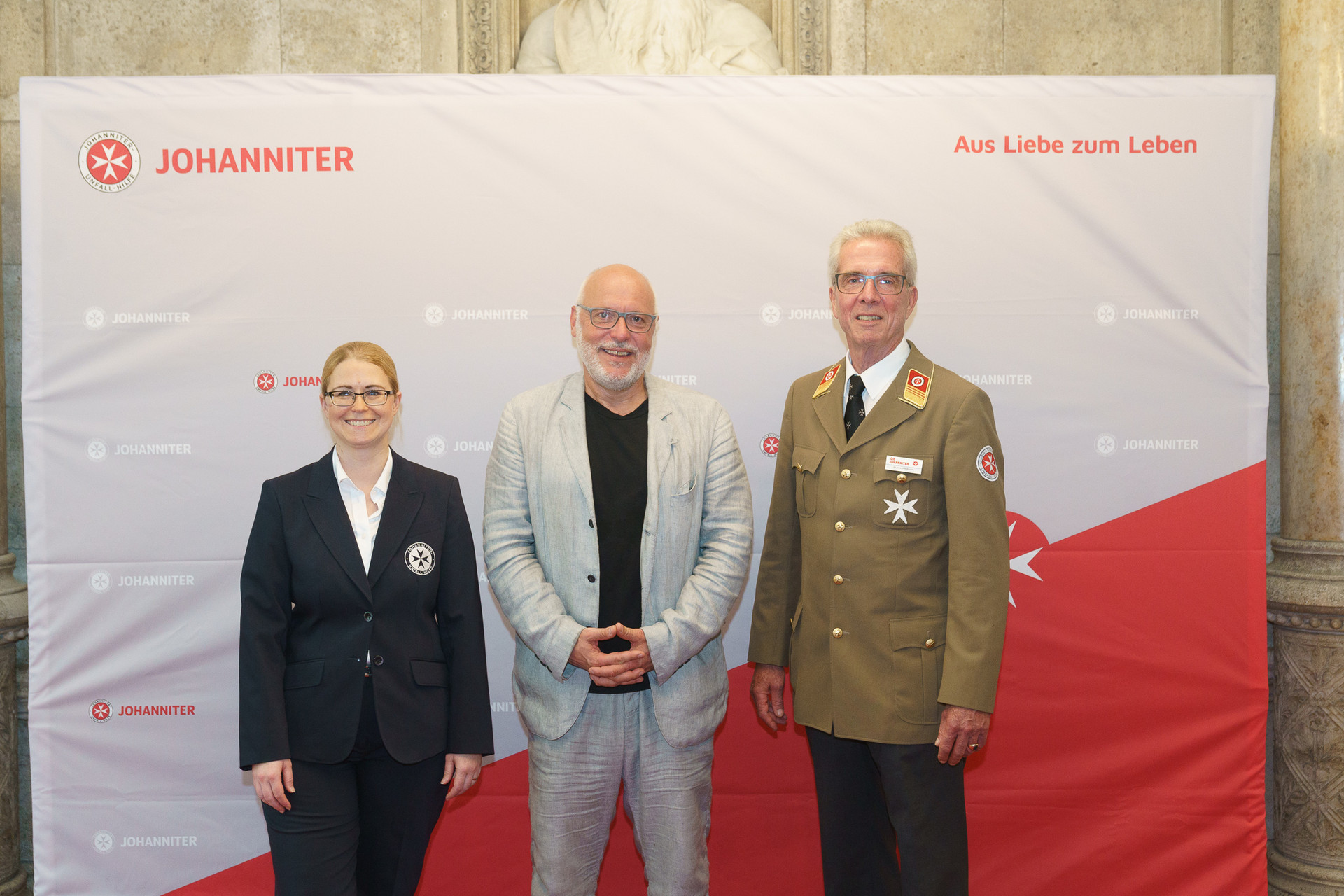 Präsident Johannes Bucher und Bundesgeschäftsführerin Petra Grell-Kunzinger mit Personen vor einer Johanniter Leinwand