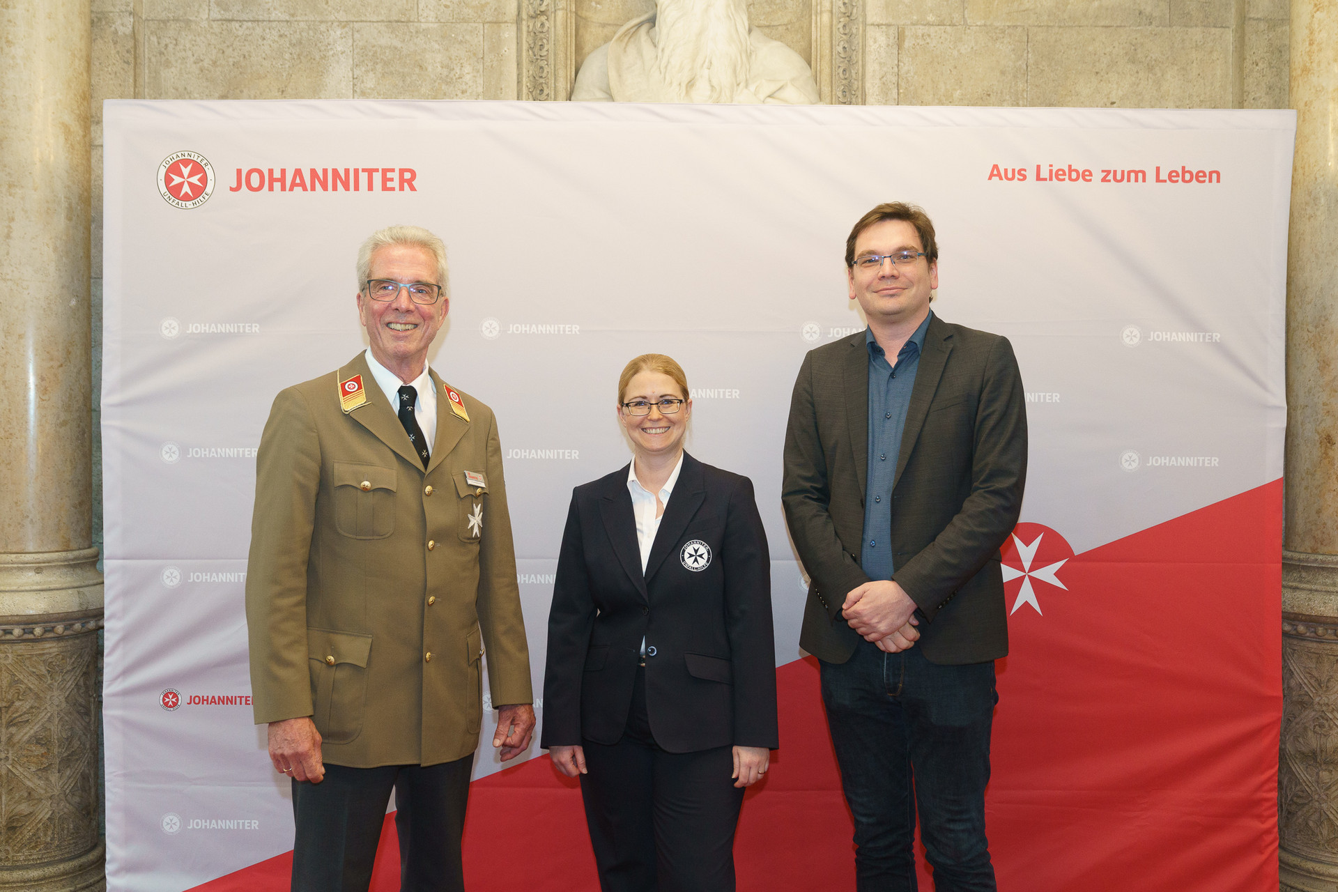 Präsident Johannes Bucher und Bundesgeschäftsführerin Petra Grell-Kunzinger mit Personen vor einer Johanniter Leinwand