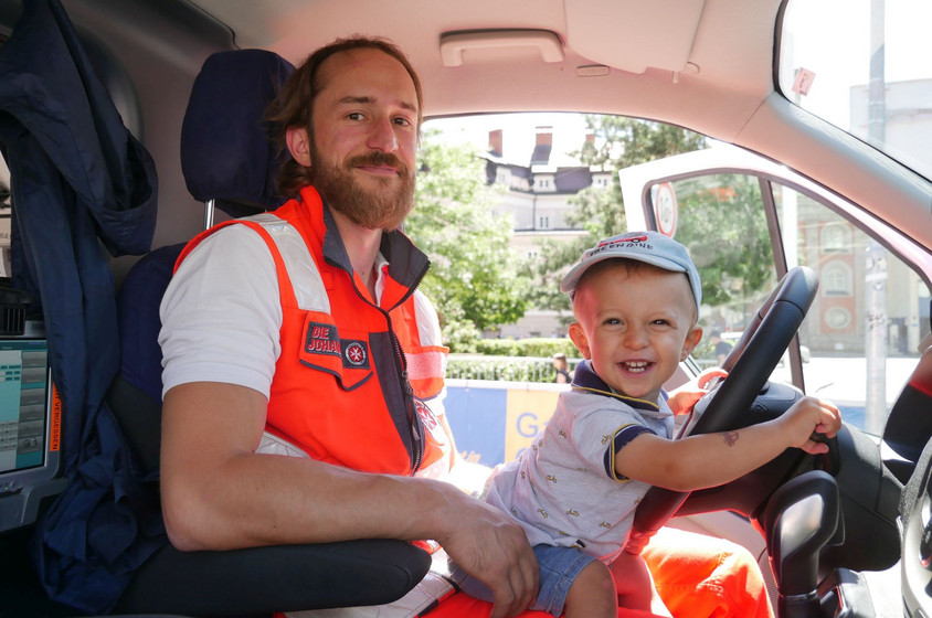 Ein kleiner Junge sitzt auf dem Schoß eines Rettungssanitäters, der hinter dem Steuer eines Rettungsautos sitzt.