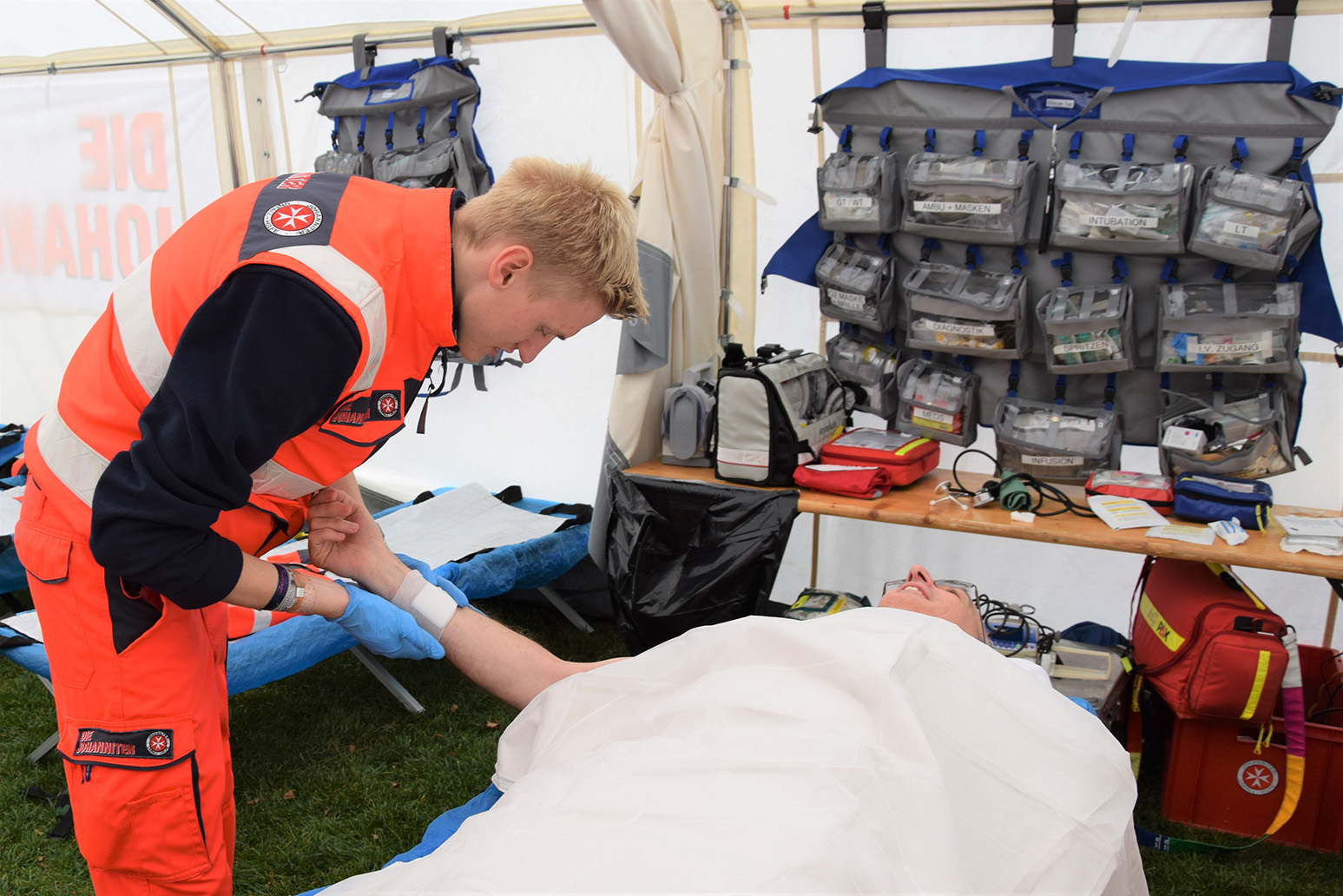 Ein Sanitäter versorgt einen Patienten, der auf einer Bahre liegt.